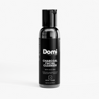 A bottle of Domi Skin Charcoal Facial Cleanser on a light gray background. The bottle is black with a black cap and a black label featuring white text.