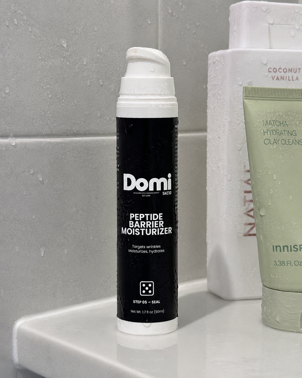 Domi Peptide Barrier Moisturizer in a black and white pump bottle, displayed on a bathroom counter next to Natii and Innisfree products.