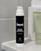 Domi Peptide Barrier Moisturizer in a black and white pump bottle, displayed on a bathroom counter next to Natii and Innisfree products.