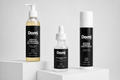 Three Domi skincare products displayed on white pedestals against a light gray background: a Gentle Hydrating Gel Cleanser bottle, a Hyaluronic Acid dropper bottle, and a Peptide Barrier Moisturizer canister.