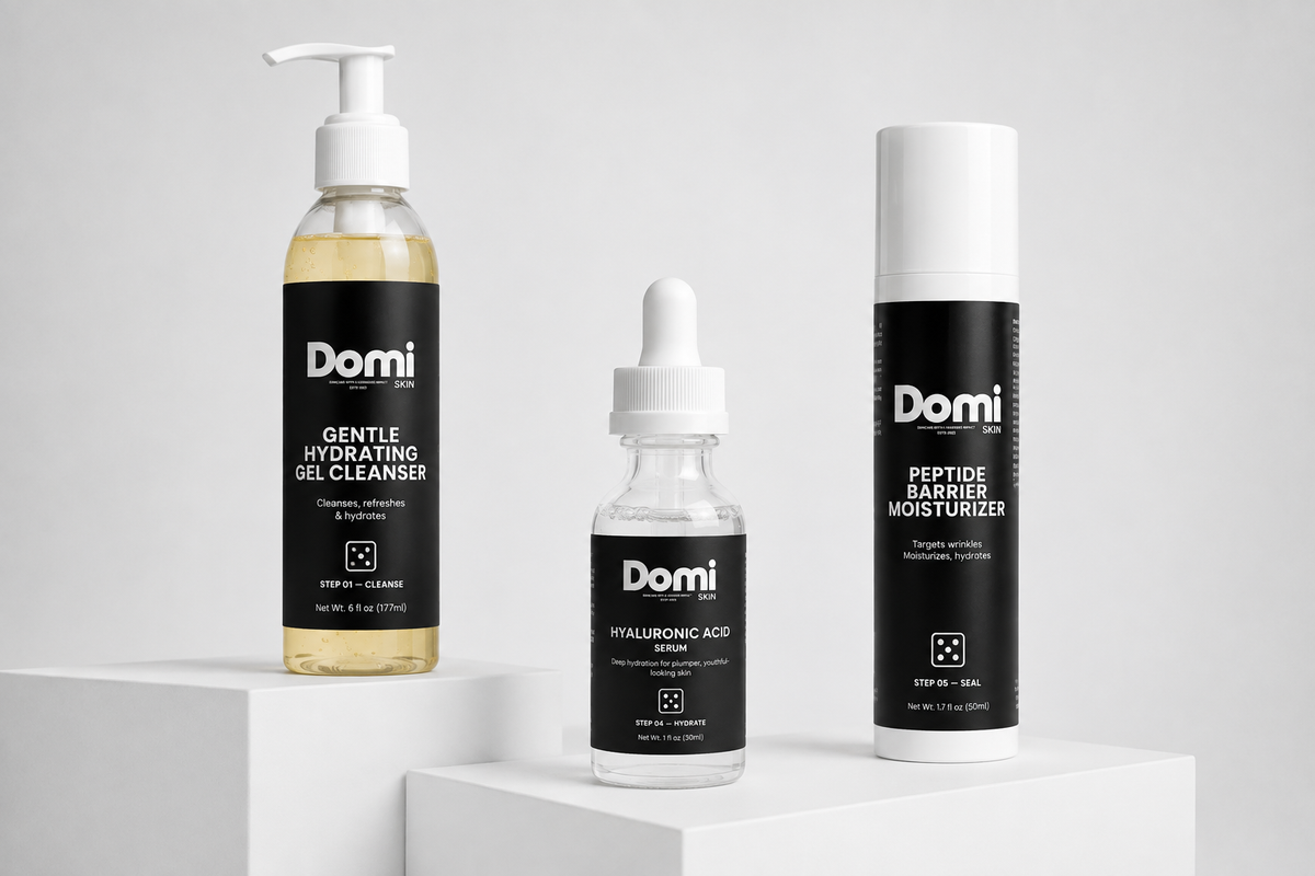 Three Domi skincare products displayed on white pedestals against a light gray background: a Gentle Hydrating Gel Cleanser bottle, a Hyaluronic Acid dropper bottle, and a Peptide Barrier Moisturizer canister.